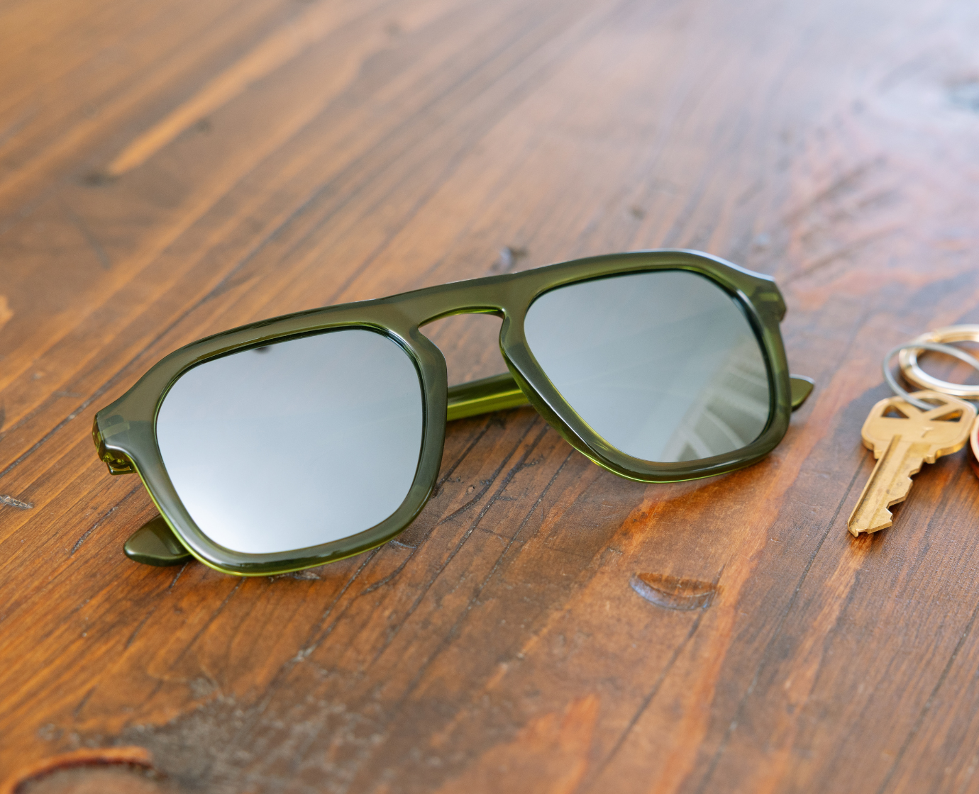 Peepers Deep Dive Sunglasses in olive green resting on a wooden table