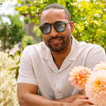 Man in a white shirt wearing Peepers Deep Dive Sunglasses in olive green in a garden