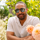Man in a white shirt wearing Peepers Deep Dive Sunglasses in olive green in a garden