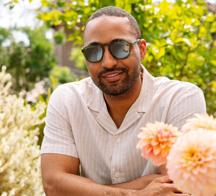 Man in a white shirt wearing Peepers Deep Dive Sunglasses in olive green in a garden