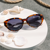 Peepers En Route Sunglasses in Tortoise/White on a white table with seashells