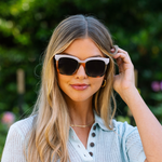 Smiling woman in a light blue top wearing Peepers Frenchy Sunglasses in Mocha Tortoise/Cream