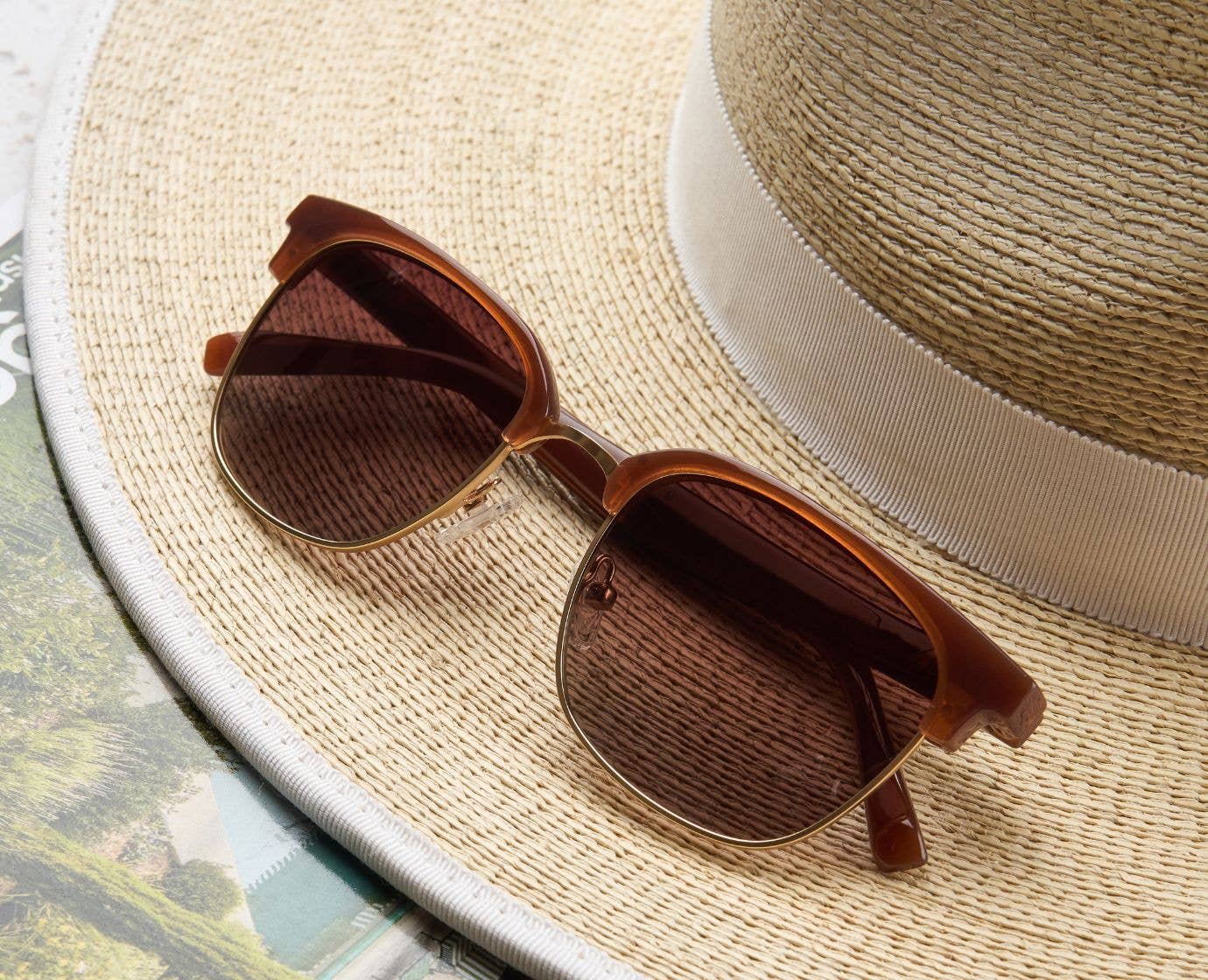 Peepers Houston Sunglasses in Brown resting on a straw hat