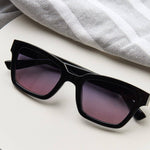 Peepers Myrtle Sunglasses in Black resting on a white surface beside a towel
