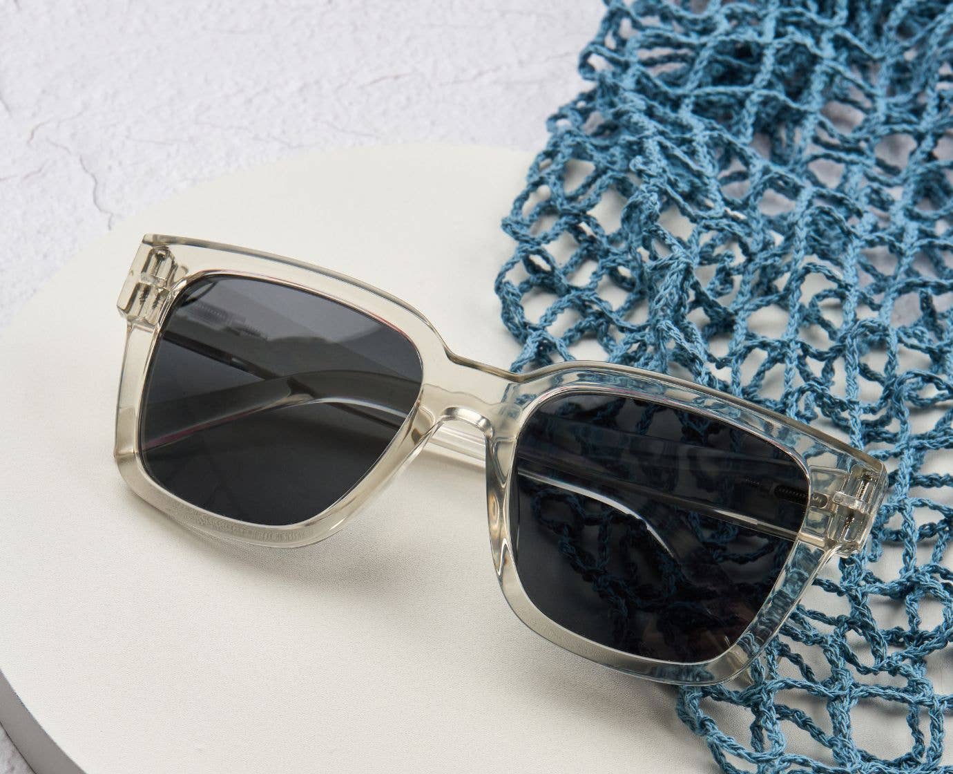 Peepers Paloma Sunglasses in Fog resting beside a blue net bag