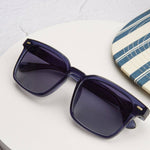 Peepers Shasta Sunglasses in Blue resting on a white table beside a striped surfboard