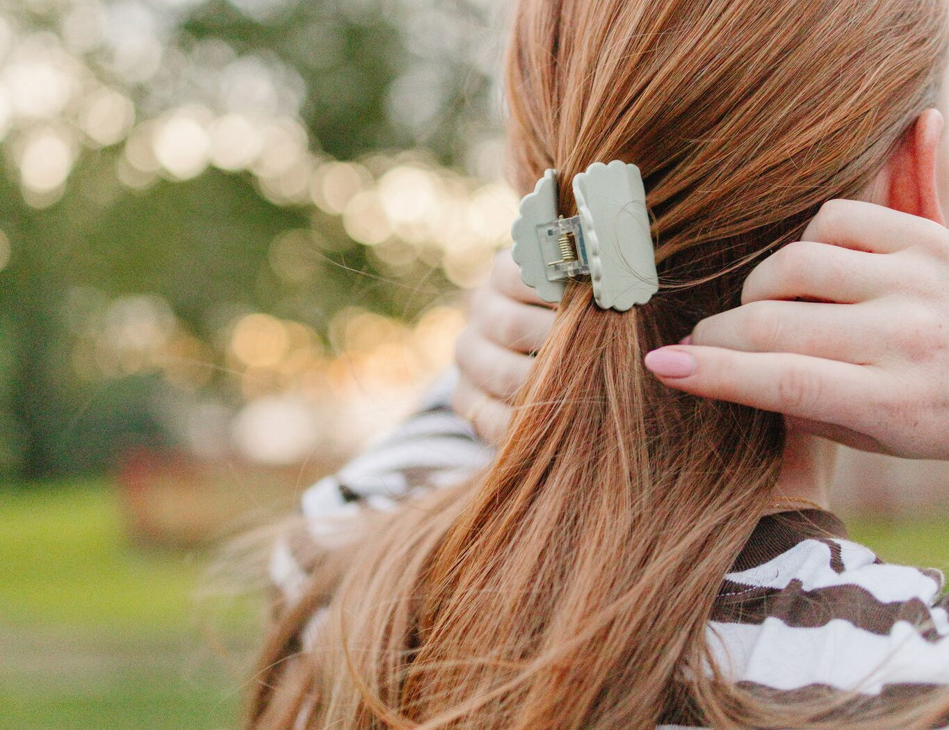 A soft sage Petal claw clip with its scalloped edge holding a low half up ponytail.