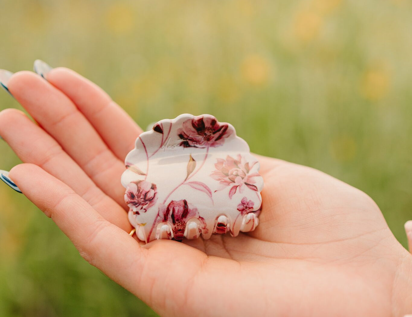 The Mulberry Floral Petal claw clip resting in an open palm, cream with a deep rose floral print.