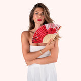 Woman in a white dress holding the Powder Designs Satin Fan in Rouge Blooms