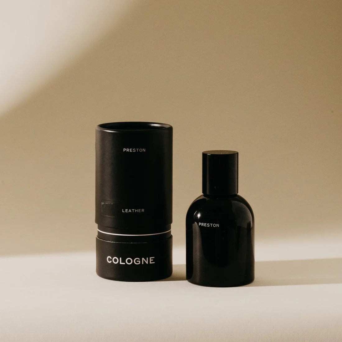 Preston Cologne matte black bottle beside its black cylinder box in warm light