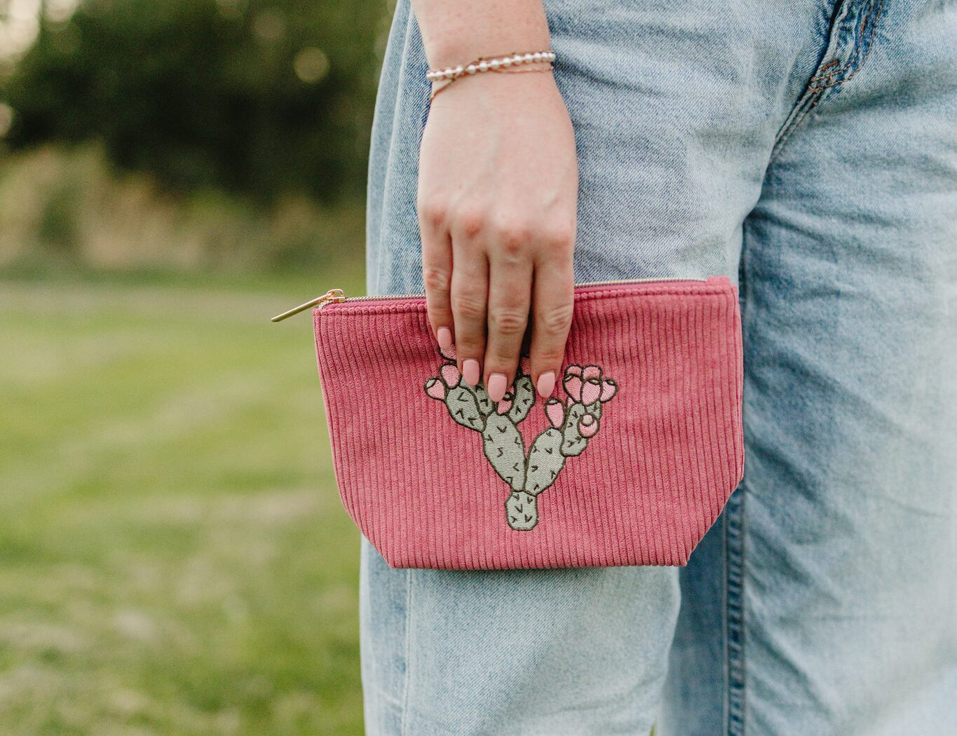 The Prickly Mauve Pear medium corduroy pouch in dusty rose with a cream prickly pear embroidery, held at the hip.