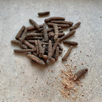 Rivsalt Java Long Pepper spikes scattered on a stone surface with ground pepper