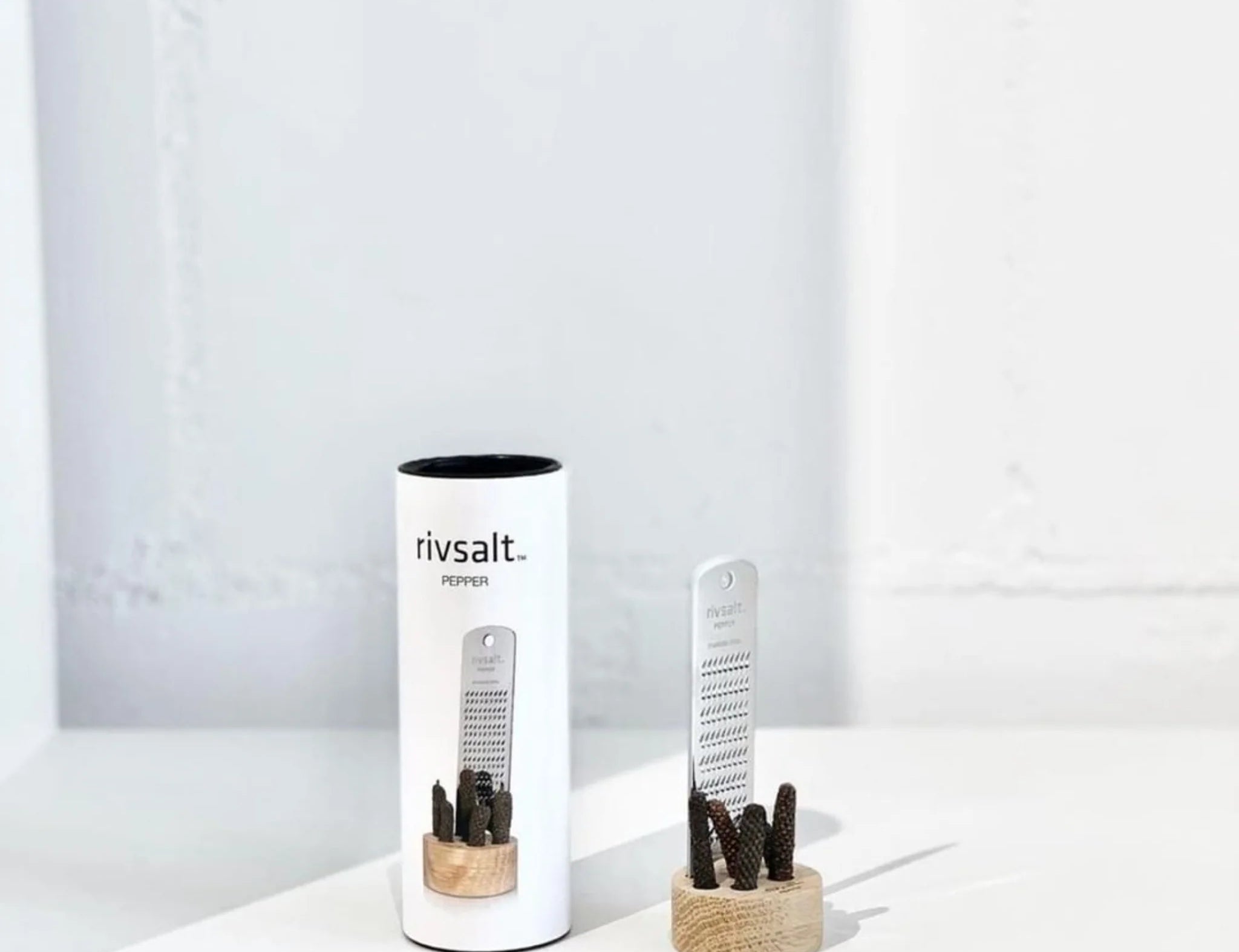 Rivsalt Pepper Stainless Steel Grater with long pepper on a wooden stand beside its white tube