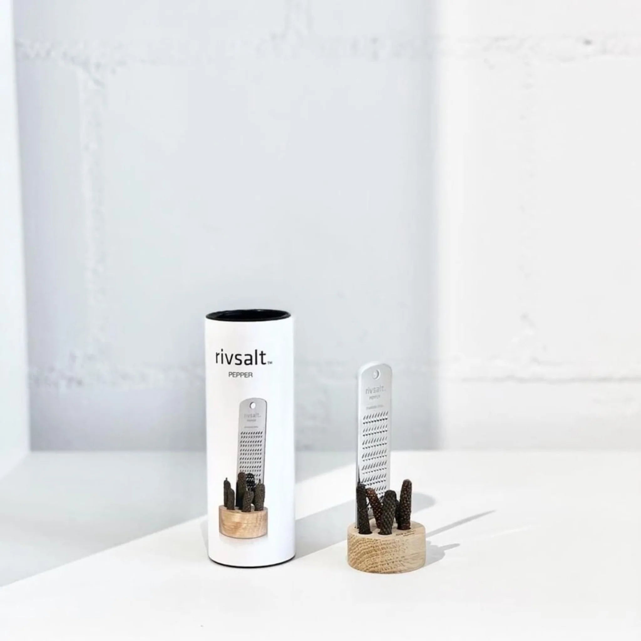 Rivsalt Pepper Stainless Steel Grater with long pepper on a wooden stand beside its white tube