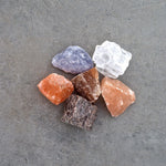 Assorted Rivsalt salt rocks in pink, purple, white and orange on a gray surface