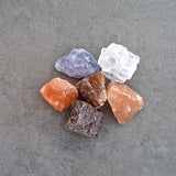 Assorted Rivsalt salt rocks in pink, purple, white and orange on a gray surface