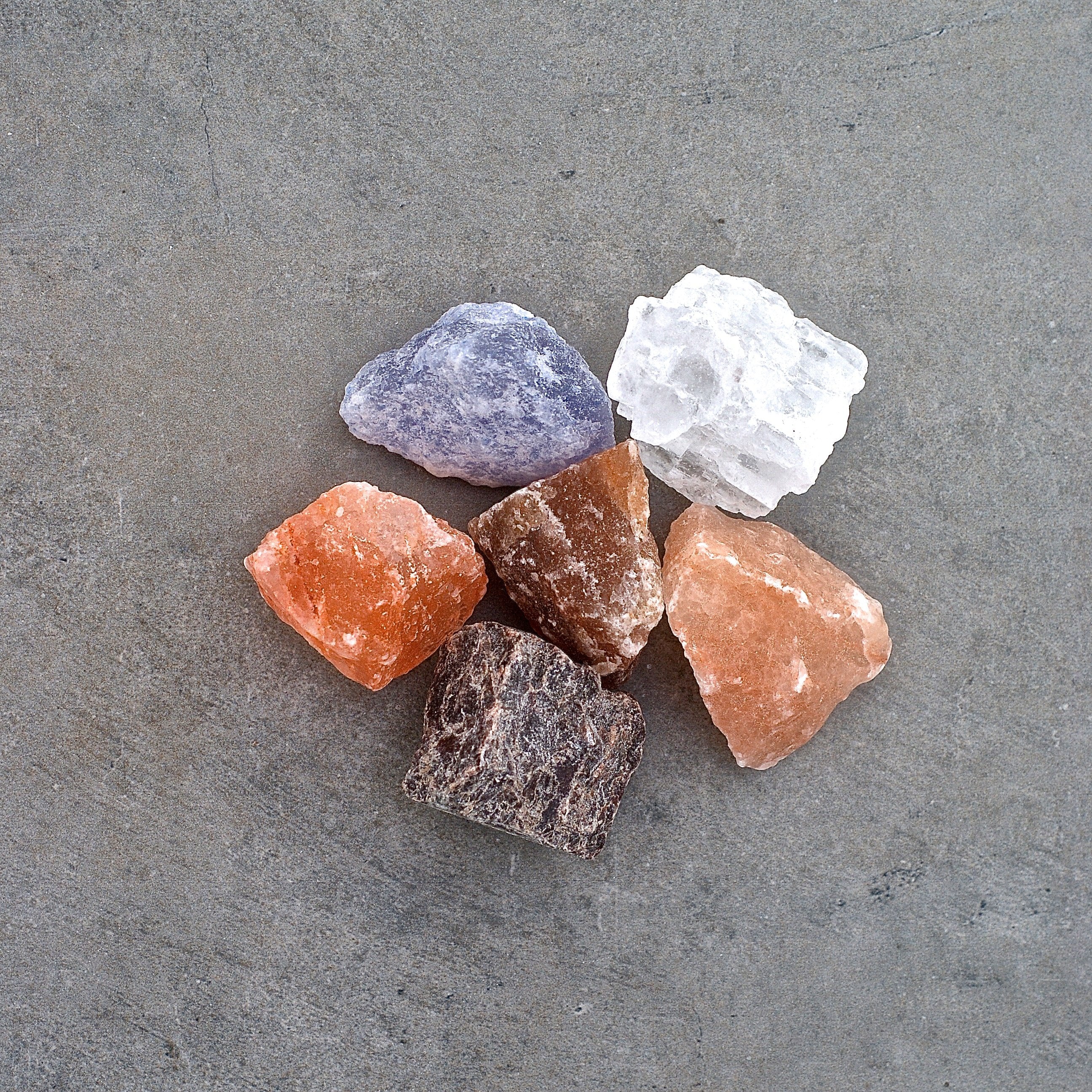 Assorted Rivsalt salt rocks in pink, purple, white and orange on a gray surface
