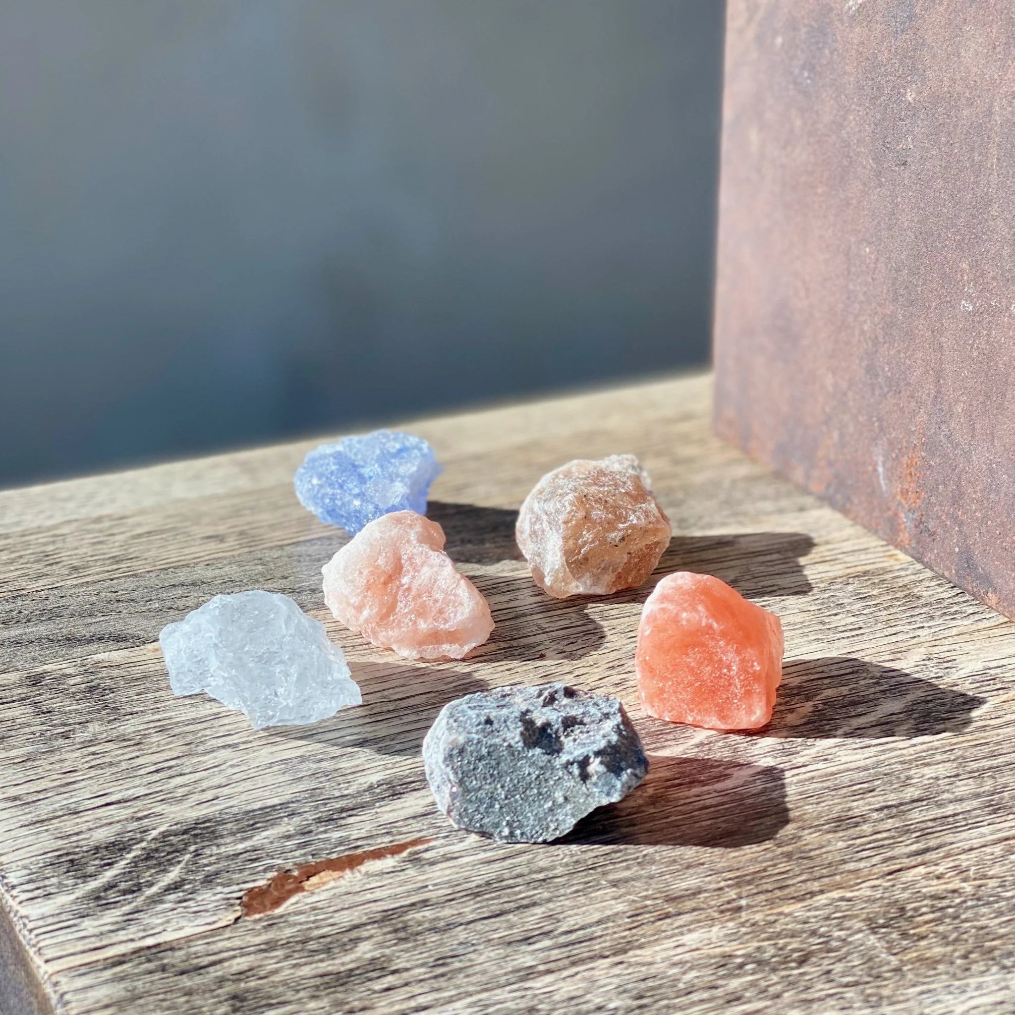 Assorted Rivsalt salt rocks in blue, pink, orange and gray on a rustic wooden table