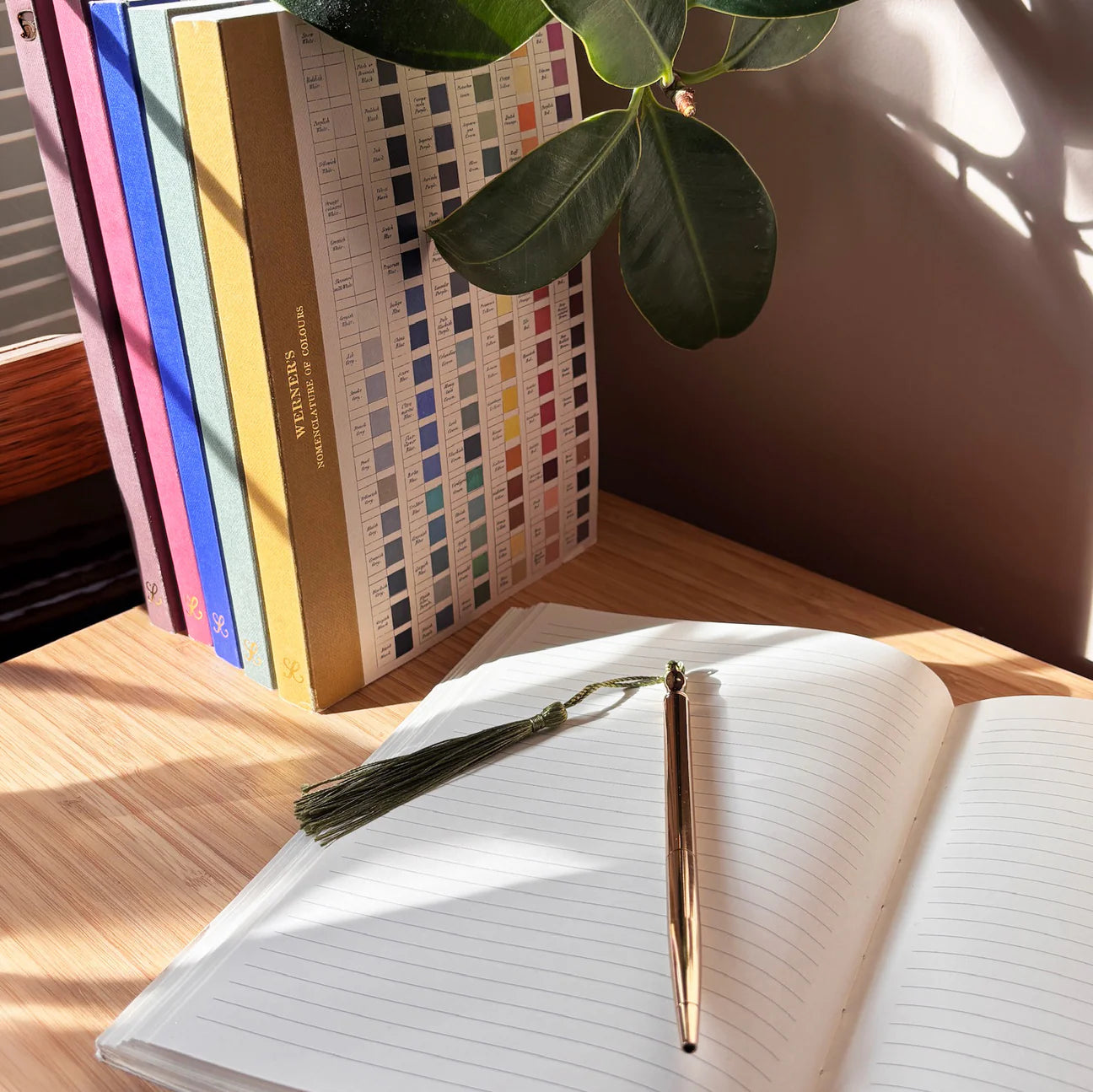 RoomyTown Lay-Flat Swan Journal open on a wooden desk with a gold pen and a plant
