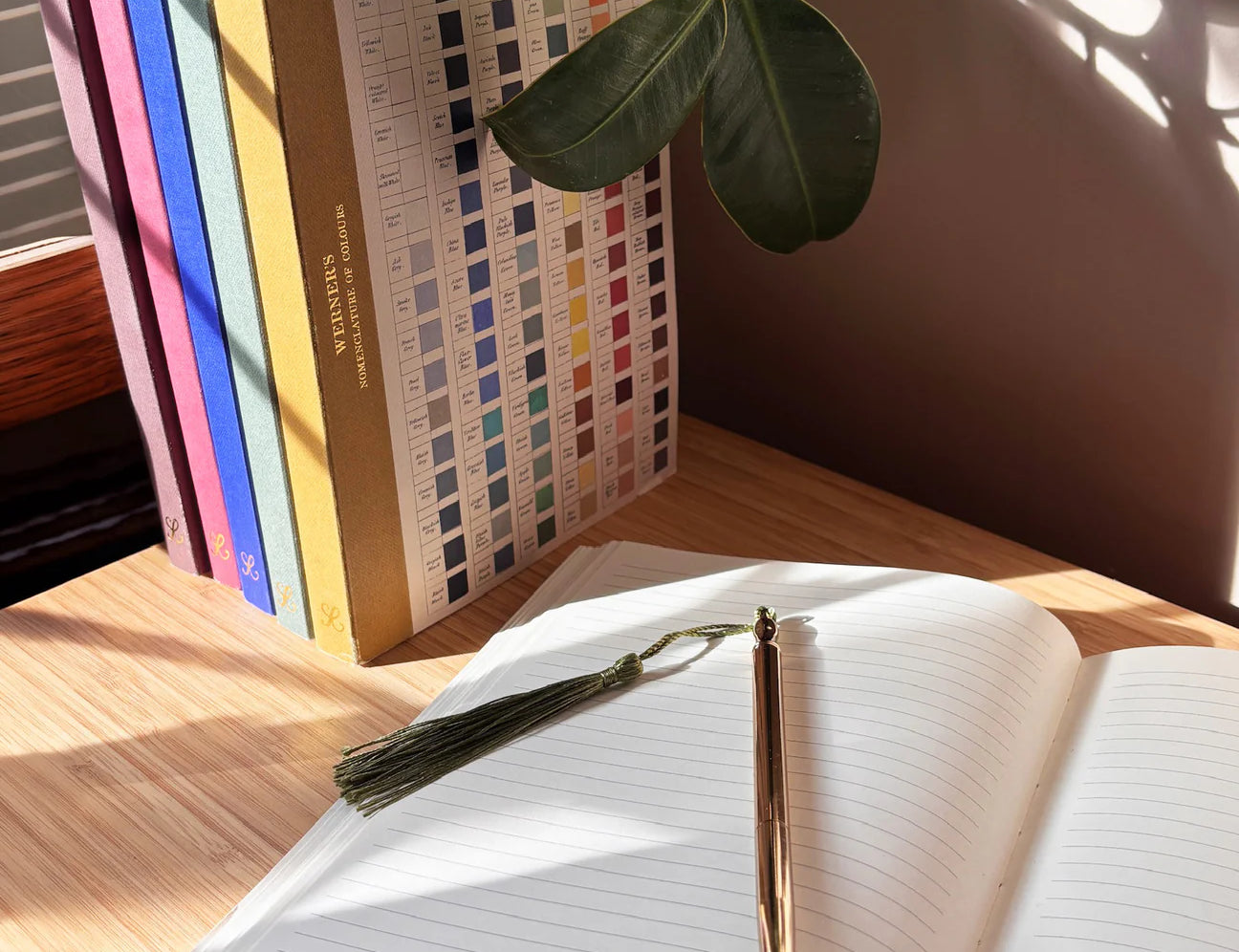 RoomyTown Lay-Flat Swan Journal open on a wooden desk with a gold pen and a plant