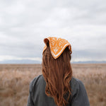 Back view of a woman with long red hair wearing the Rooted & Wild Adventure Co. Burn and Bloom Bandana as a head scarf