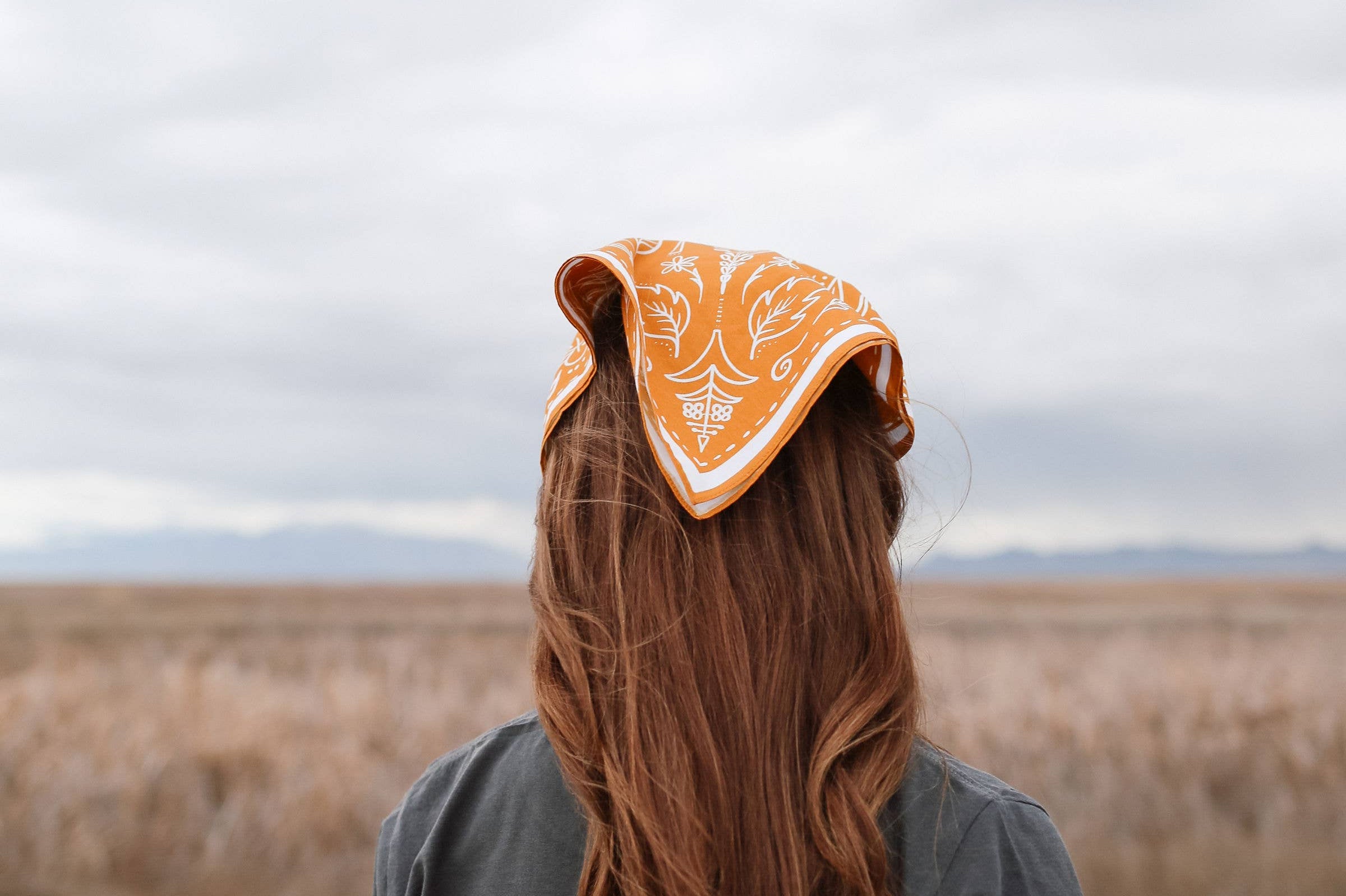 Back view of a woman with long red hair wearing the Rooted & Wild Adventure Co. Burn and Bloom Bandana as a head scarf