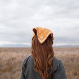 Back view of a woman with long red hair wearing the Rooted & Wild Adventure Co. Burn and Bloom Bandana as a head scarf