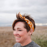 Smiling woman with short hair wearing the Rooted & Wild Adventure Co. Burn and Bloom Bandana as a headband