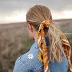 Rooted & Wild Adventure Co. Burn and Bloom Bandana tied around a blonde ponytail, worn with a denim jacket