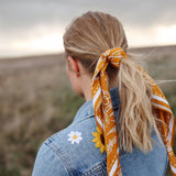 Rooted & Wild Adventure Co. Burn and Bloom Bandana tied around a blonde ponytail, worn with a denim jacket
