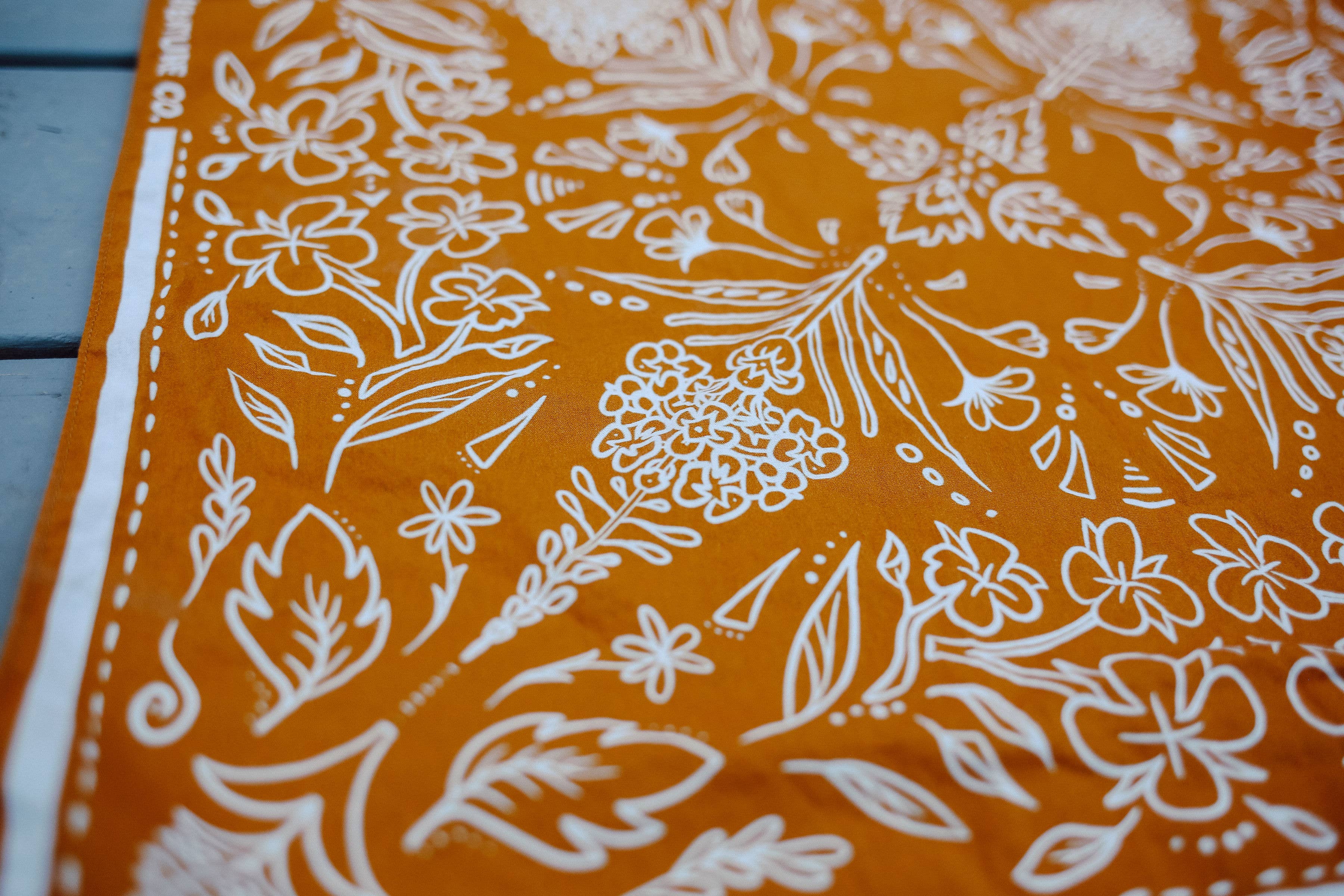 Close-up of the white wildflower print on the rust Rooted & Wild Adventure Co. Burn and Bloom Bandana