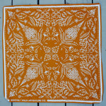 Rooted & Wild Adventure Co. Burn and Bloom Bandana, a rust orange bandana with a white wildflower print, laid flat