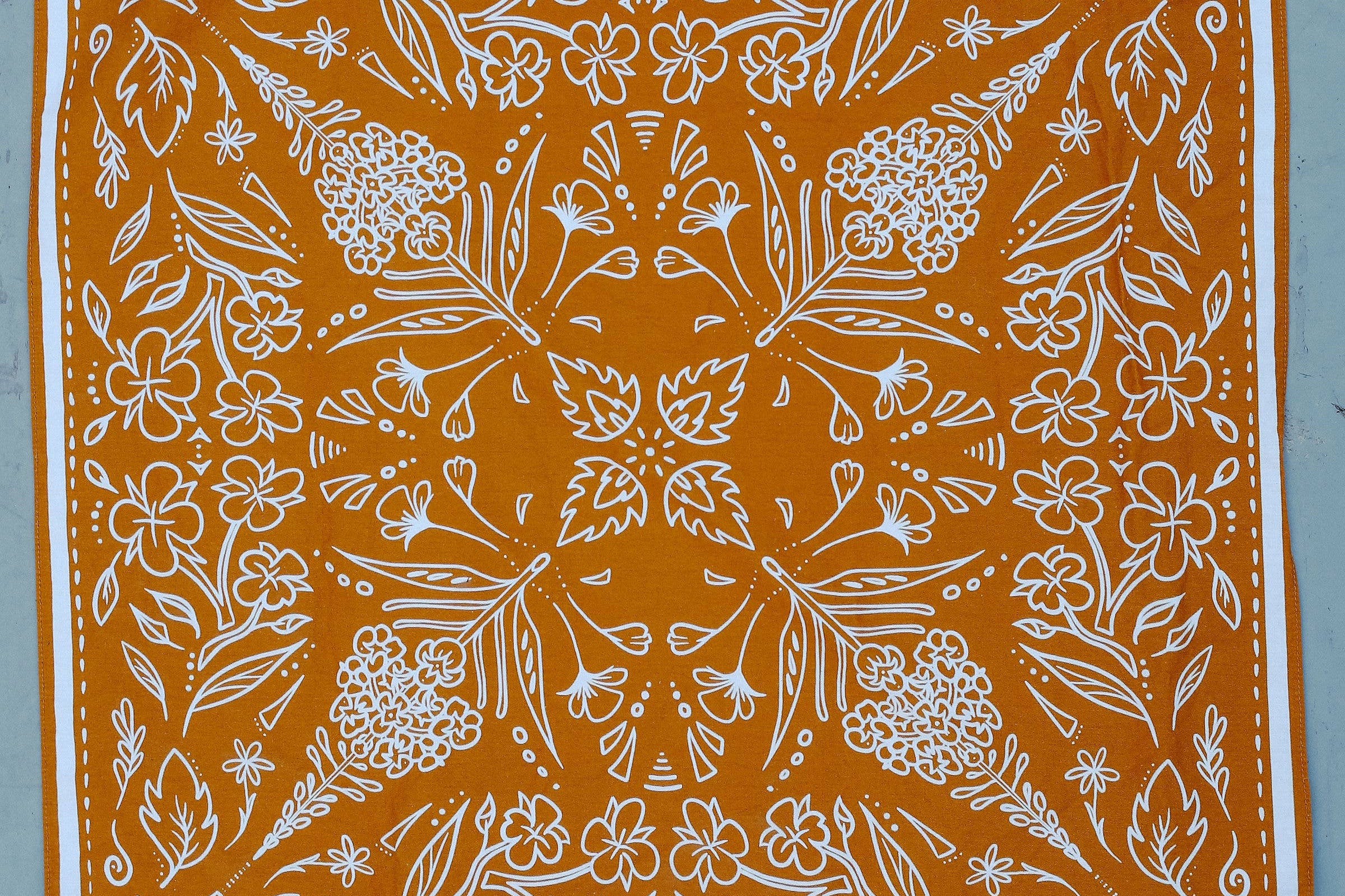 Rooted & Wild Adventure Co. Burn and Bloom Bandana, a rust orange bandana with a white wildflower print, laid flat