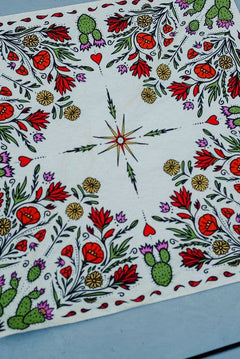 Rooted & Wild Adventure Co. Desert Bloom Bandana, a cream bandana with red cactus flowers and green botanicals, laid flat on blue wood