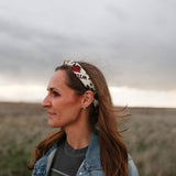 Woman in a denim jacket wearing the Rooted & Wild Adventure Co. Desert Bloom Bandana as a headband in a field