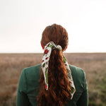 Back view of a woman with long red hair wearing the Rooted & Wild Adventure Co. Desert Bloom Bandana in her ponytail