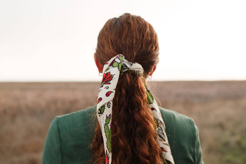 Back view of a woman with long red hair wearing the Rooted & Wild Adventure Co. Desert Bloom Bandana in her ponytail