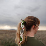 Rooted & Wild Adventure Co. Desert Bloom Bandana tied around a blonde ponytail under a stormy sky
