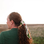 Woman in a green top wearing the Rooted & Wild Adventure Co. Desert Bloom Bandana in her hair, side view