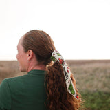 Woman in a green top wearing the Rooted & Wild Adventure Co. Desert Bloom Bandana in her hair, side view