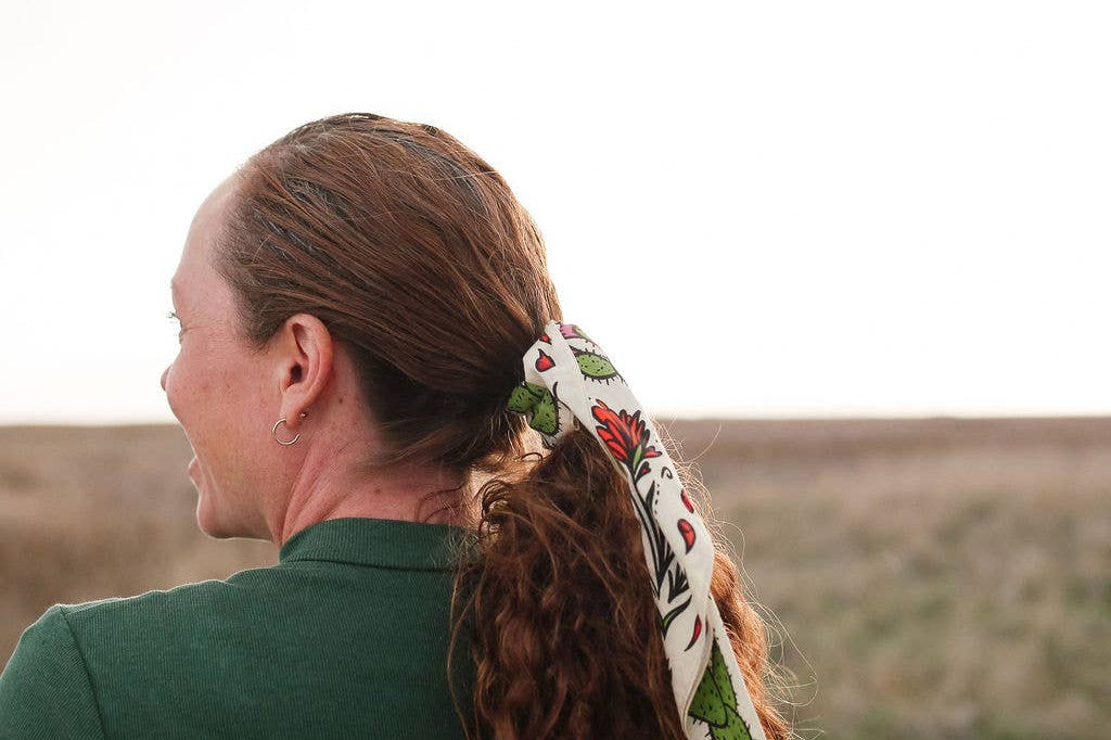 Woman in a green top wearing the Rooted & Wild Adventure Co. Desert Bloom Bandana in her hair, side view