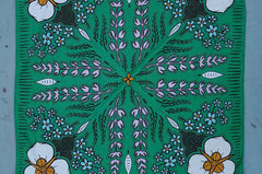 Rooted & Wild Adventure Co. High Meadows Bandana, green with a wildflower print, laid flat on blue wood