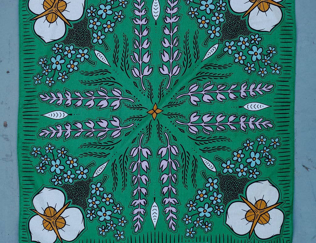 Rooted & Wild Adventure Co. High Meadows Bandana, green with a wildflower print, laid flat on blue wood
