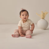 Rylee & Cru Baby Pant in Blush worn by a seated baby in a cream top beside a vase of dried grass