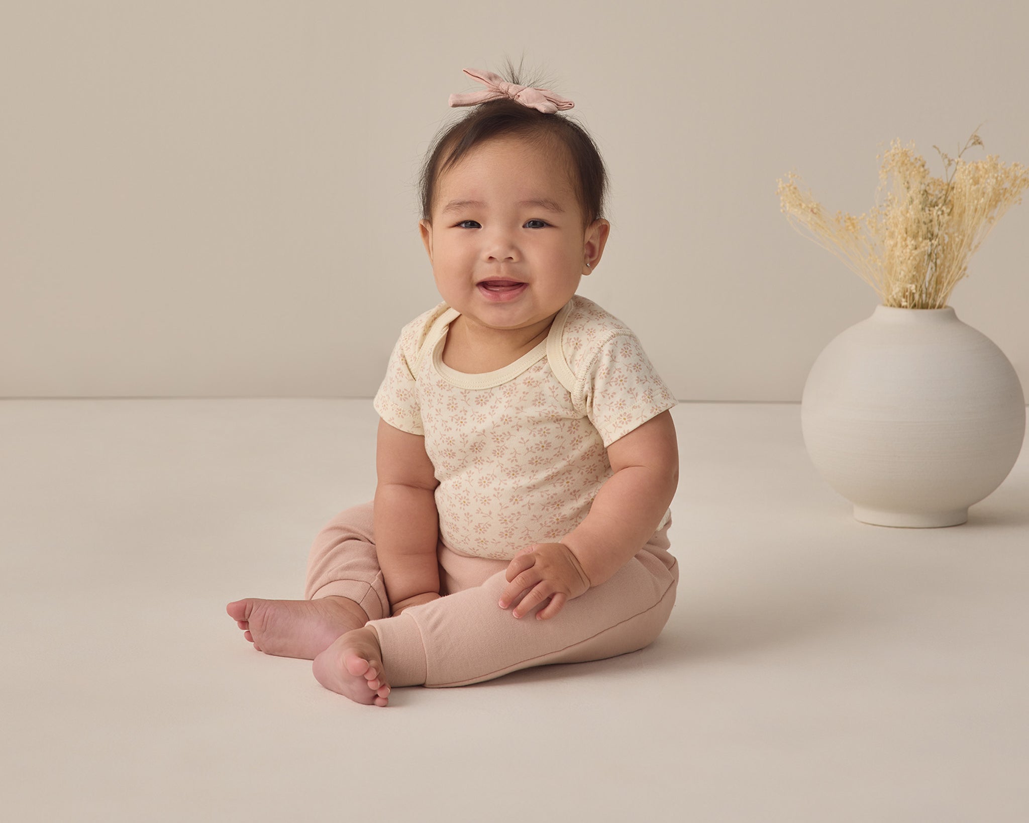 Rylee & Cru Baby Pant in Blush worn by a smiling seated baby in a cream top
