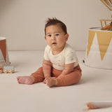 Rylee & Cru Baby Pant in Poppy worn by a seated baby in a cream top with a party garland behind