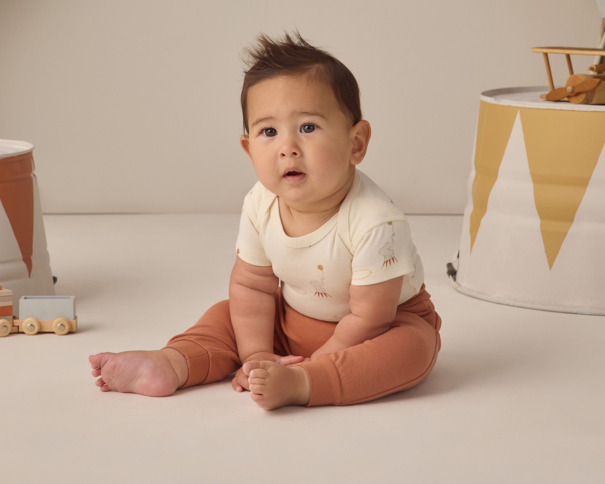 Rylee & Cru Baby Pant in Poppy worn by a seated baby in a cream top with a party garland behind