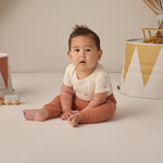 Rylee & Cru Baby Pant in Poppy rust worn by a seated baby looking at the camera