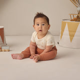 Rylee & Cru Baby Pant in Poppy rust worn by a seated baby looking at the camera