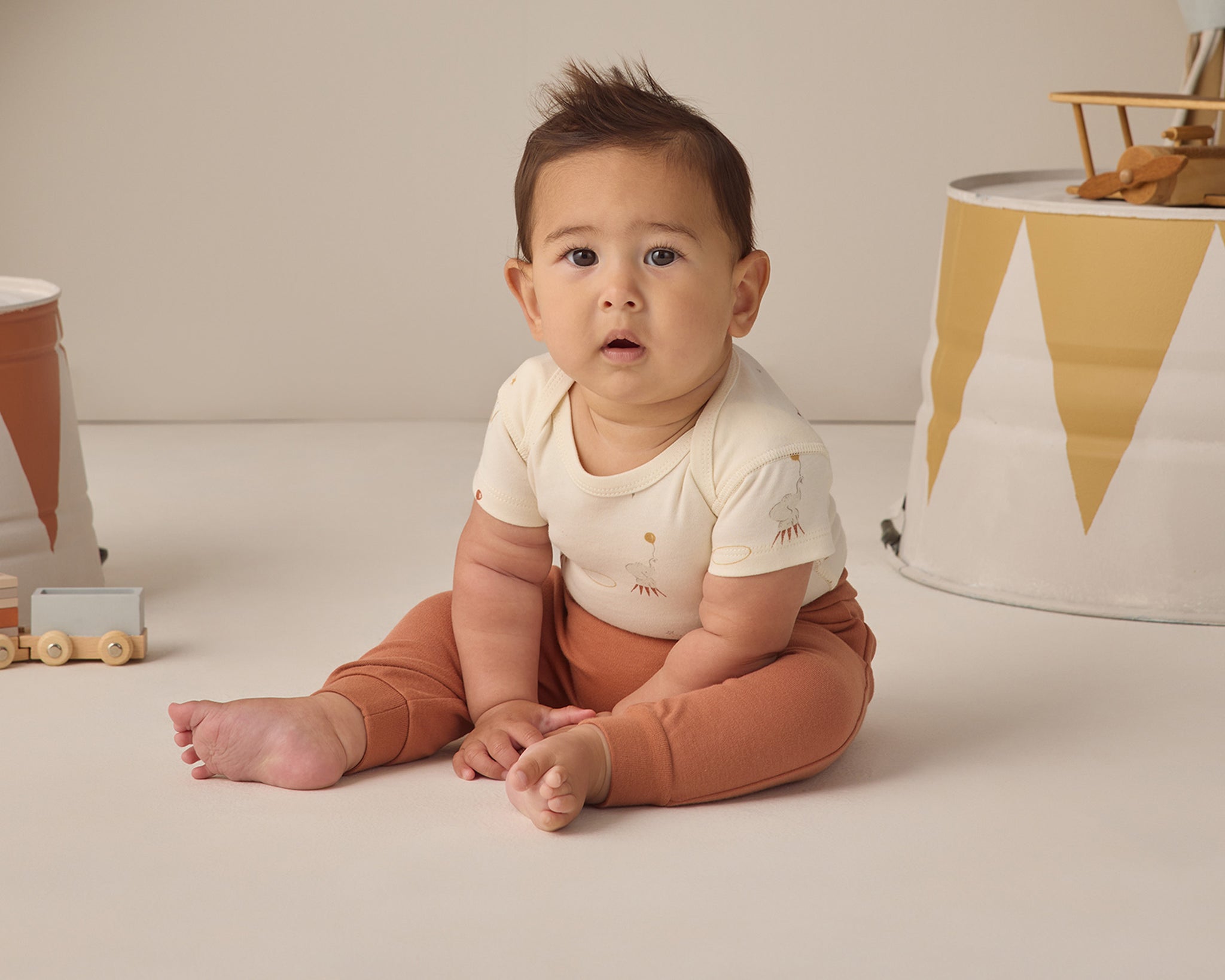 Rylee & Cru Baby Pant in Poppy rust worn by a seated baby looking at the camera
